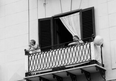 A black and white photo of an elderly couple on an Italian balcony enjoying the day.