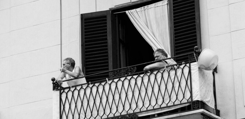 A black and white photo of an elderly couple on an Italian balcony enjoying the day.